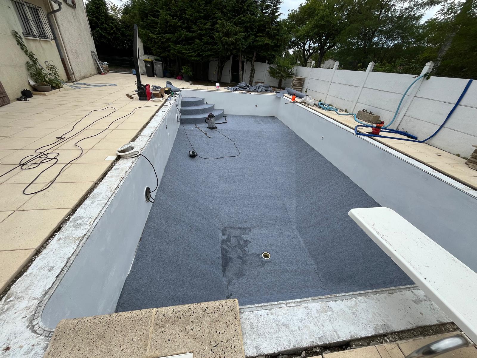 Feutre géotextile gris en cours de pose sur le fond du bassin